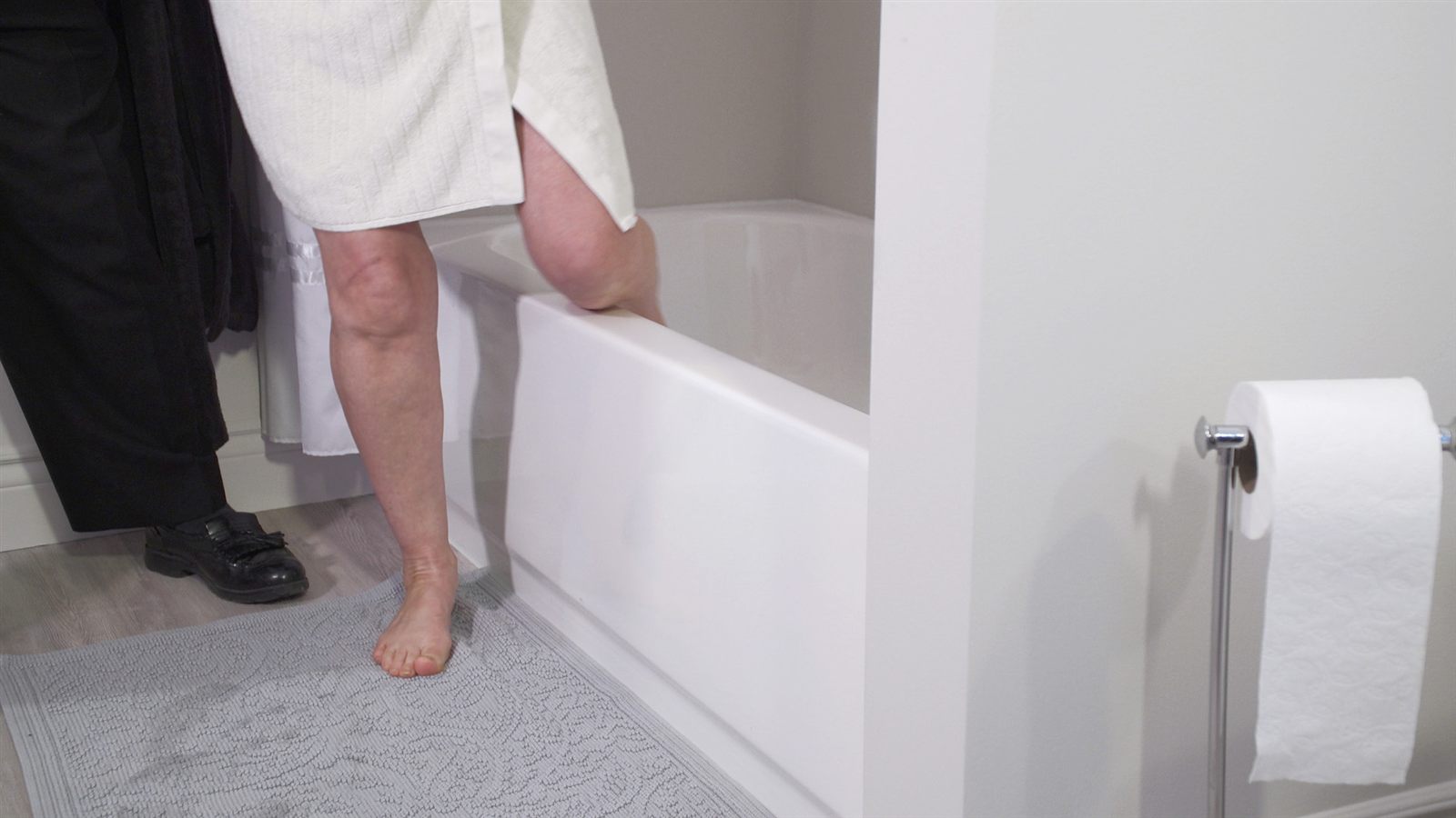 A person carefully lifting their leg over a high bathtub wall